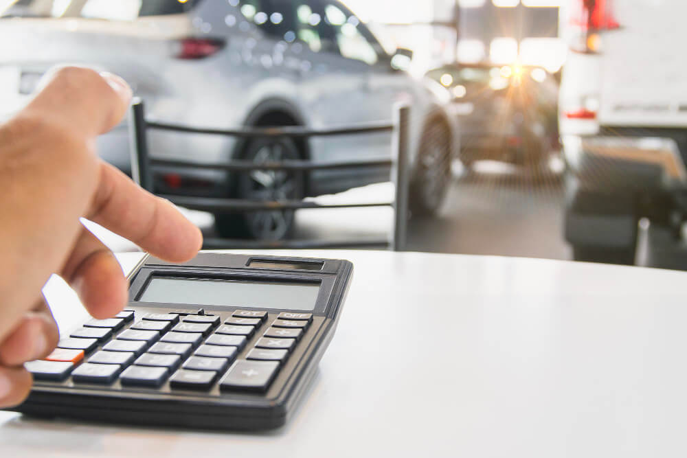 Eine Hand tippt im Autohaus auf einen Taschenrechner und berechnet einen Kostenvoranschlag nach Unfallgutachten