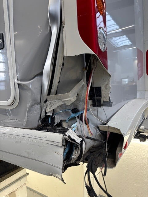 Das hintere Eck eines beschädigten Wohnmobils mit freiliegenden Kabeln, eingedrücktem Metall und zerstörtem Paneel für Unfallgutachten