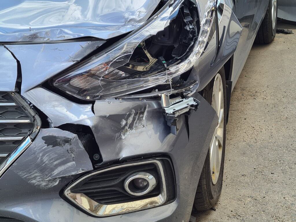 Ein silbernes Auto mit starken Schäden an Frontscheinwerfer, Stoßstange und Kotflügel rechts vorne, automatisch gespeicherter Entwurf